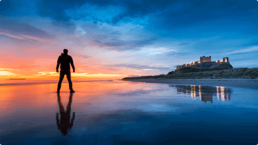 A person standing on Bamburgh beach with the castle in the background