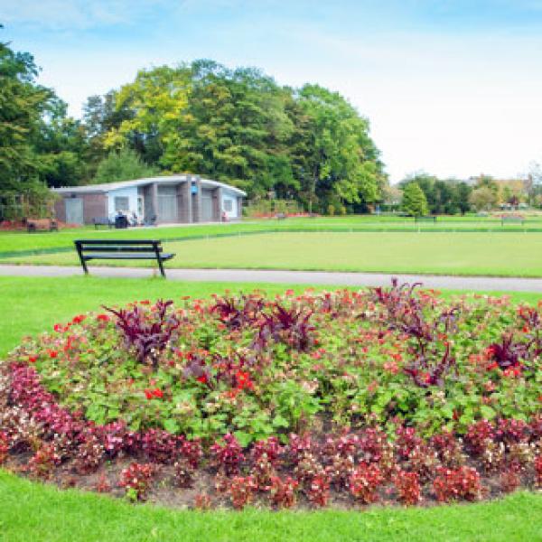 A round flower bed with various flowers and a large open grass space behind.