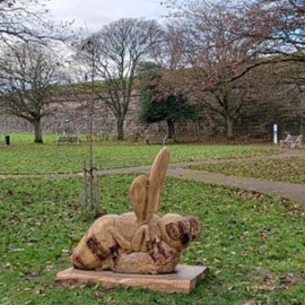 A large grass area with trees scattered around. Close to the camera is a large carved wooden statue of a Honeybee