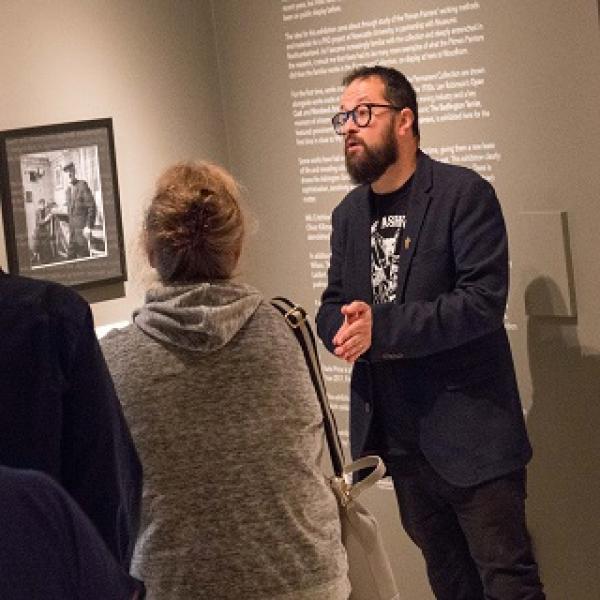 A man at the front of a group talking about one of the exhibitions at a museum.