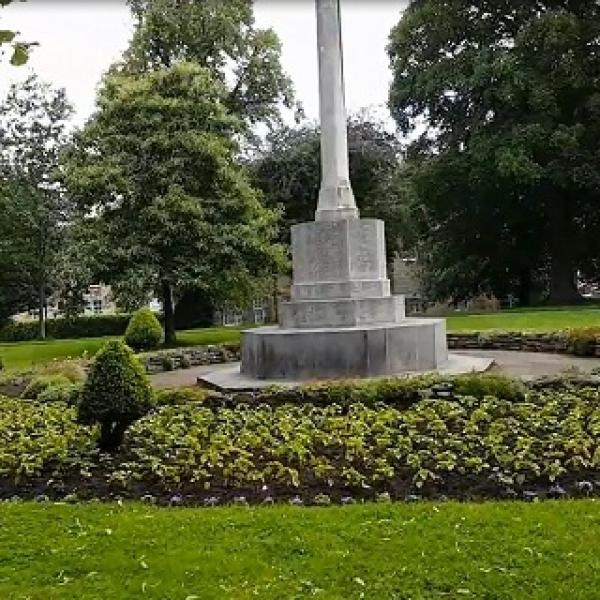 A large stone pillar memorial surrounded by flower beds.