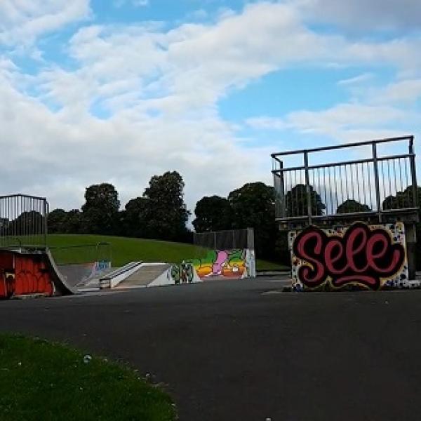 A skate park with various ramps. Graffiti is on the back of one ramp, the word "Sele"
