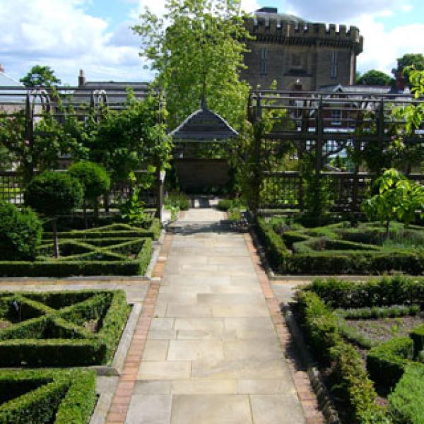 a paved pathway with slabs with well trimmed bushes lining the side. A wooden structure stands at the end.